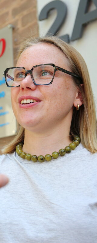 Eine Frau übergibt einen Schlüssel an eine Person. Die Person, die den Schlüssel bekommt, sieht man von hinten.