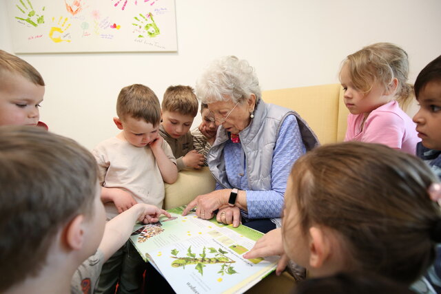 Eine ältere Frau schaut sich gemeinsam mit kleinen Kindern ein Buch an.