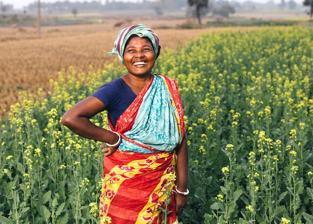 Indigene Kleinbäuerin in Bangladesch. Sie steht in einem Feld und lacht 
