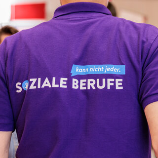 Karriere Ein Mensch von hinten, auf seinem T-Shirt Rücken steht "Soziale Berufe - kann nicht jeder"