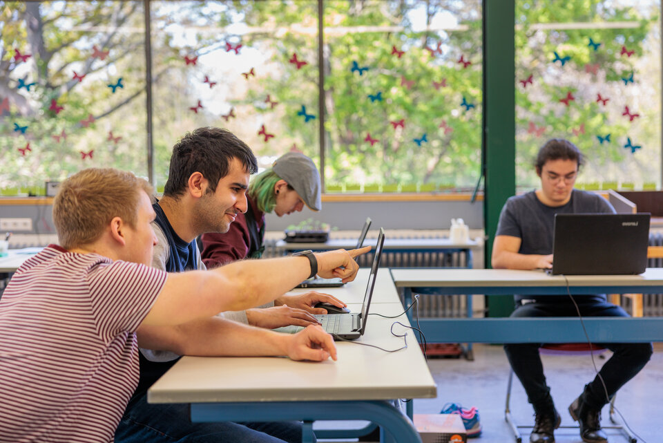 Fachverband Diakonische Schulen Junge Menschen sitzen in einem Schulraum, einer zeigt einem anderen etwas auf dem Laptop