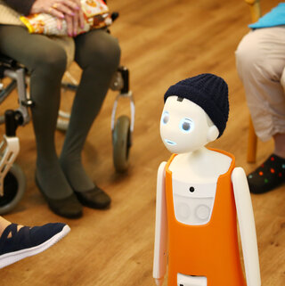 Digitalisierung und soziale Innovation Der Roboter Navel steht zwischen sitzenden Menschen in einem Altenheim