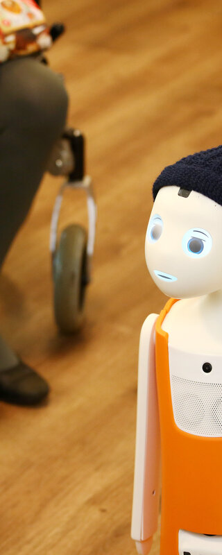 Digitalisierung und soziale Innovation Der Roboter Navel steht zwischen sitzenden Menschen in einem Altenheim