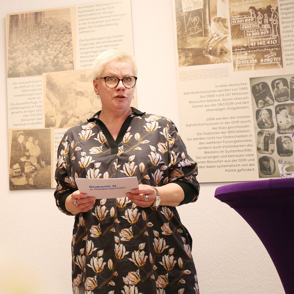 Marion Timm steht vor Bildern der Ausstellung und hält ein Grußwort