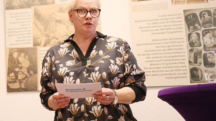 Marion Timm steht vor Bildern der Ausstellung und hält ein Grußwort