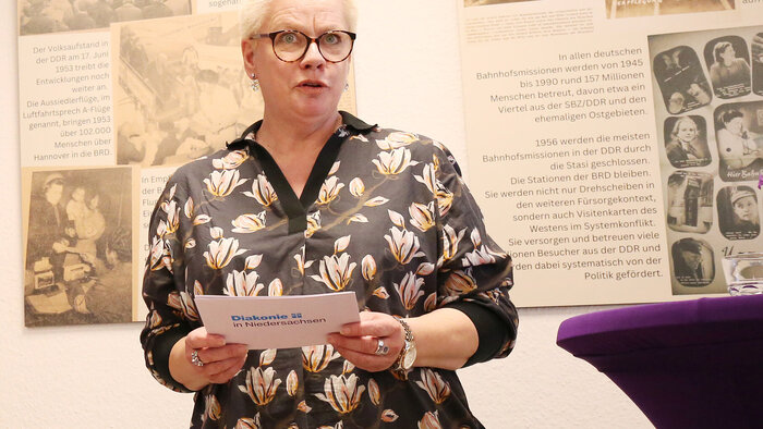 Marion Timm steht vor Bildern der Ausstellung und hält ein Grußwort