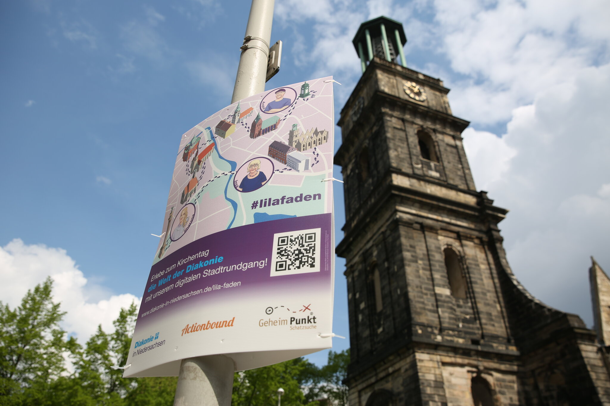 Plakat, das für den Lila Faden wirbt im Vordergrund, im Hintergrund die Aegidienkirche Hannover