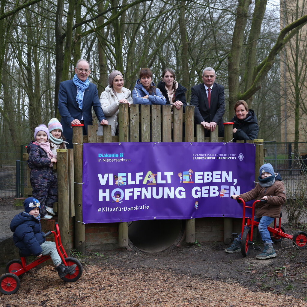 Die Teilnehmer*innen der Pressekonferenz stehen auf einem Spielplatz. Auf einem Spielgerät hängt das Plakat mit dem Slogan der Kampagne