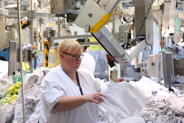 Janine Mill steht in der Wäscherei. Sie hängt ein Kleidungsstück auf einen Kleiderbügel.