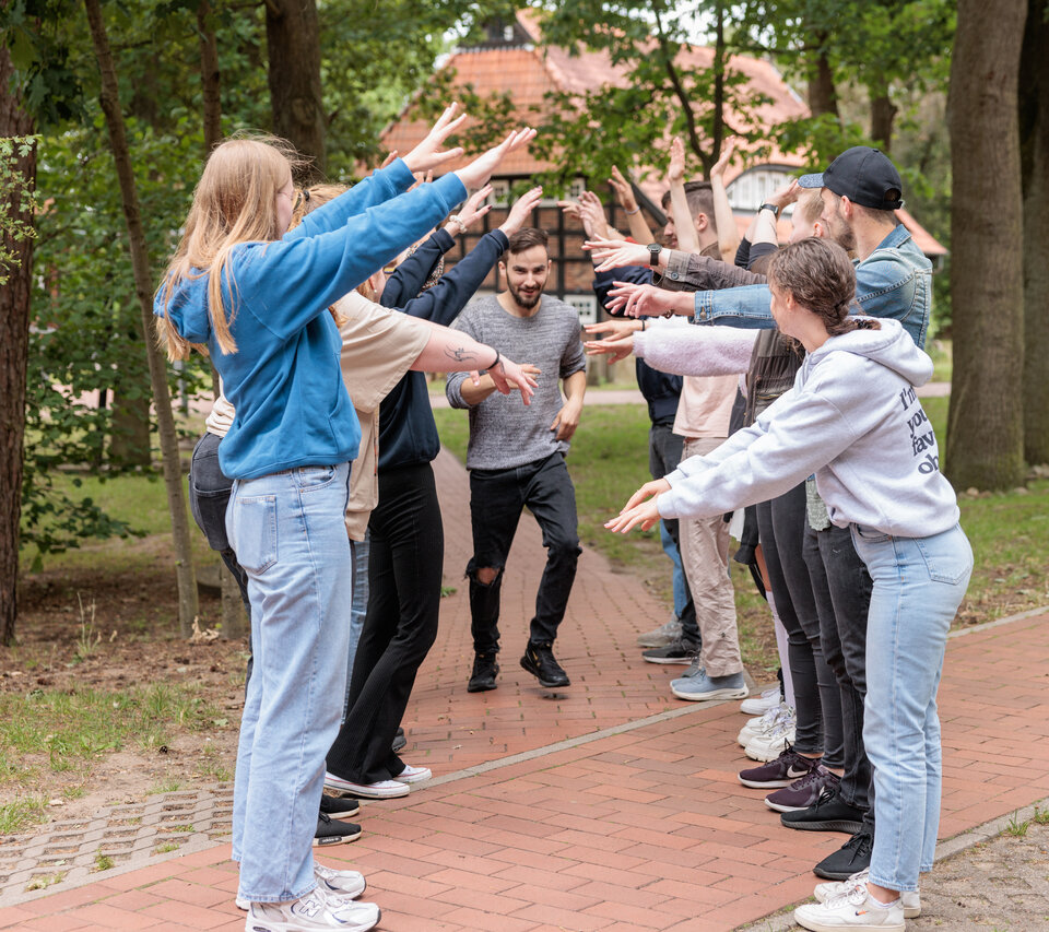 Freiwilligendienste Junge Menschen bilden ein Spalier mit ihren Armen, ein anderer junger Mensch läuft unter ihren Armen hindurch