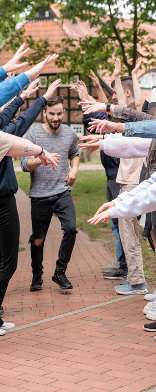 Junge Menschen bilden ein Spalier mit ihren Armen, ein anderer junger Mensch läuft unter ihren Armen hindurch