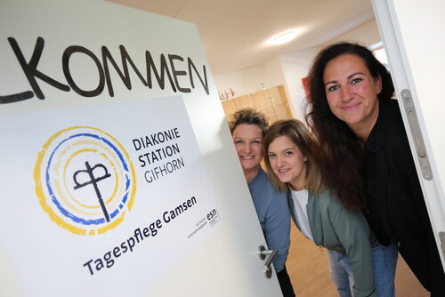 Birte Gessel, Bianca Pütsch und Janina Schoon stehen nebeneinander und schauen fröhlich in die Kamera. Neben ihnen steht ein Schild mit der Aufschrift "Willkommen"