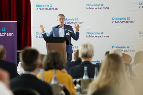 Thomas Hofer auf der Bühne der Mitgliederversammlung, im Vordergrund sieht man Teile des Plenums von hinten