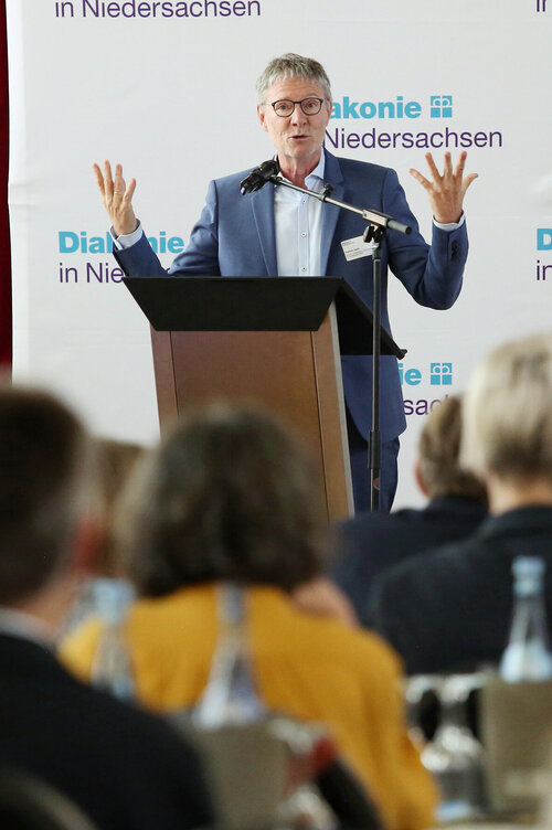 Thomas Hofer auf der Bühne der Mitgliederversammlung, im Vordergrund sieht man Teile des Plenums von hinten