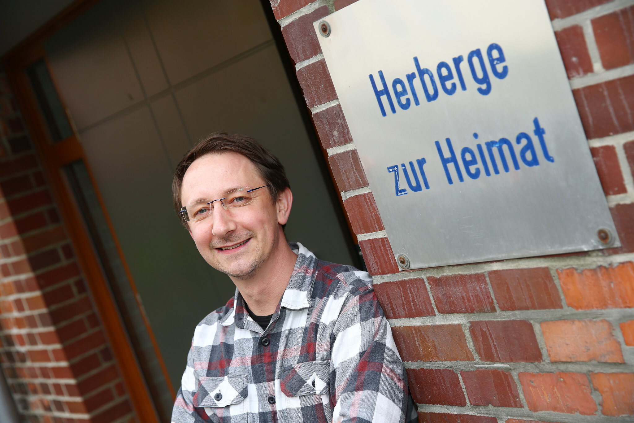 Tobias Göhl steht neben dem Schild der Herberge zur Heimat. Er schaut freundlich in die Kamera.