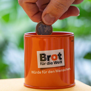 Man sieht eine Hand, die von oben eine Münze in eine Brot für die Welt Spendendose wirft