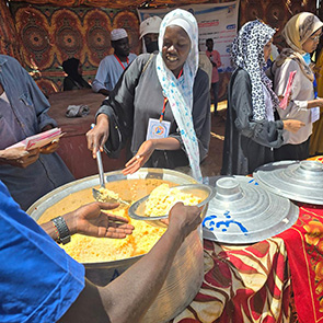Eine Person gibt anderen Person Essen aus einem großen Topf
