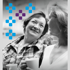 Zwei Frauen sitzen zusammen und trinken Kaffee, sie schauen sich freundlich an