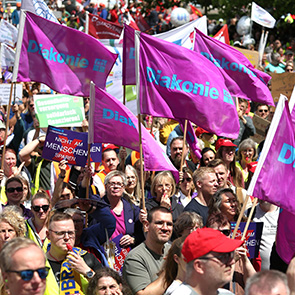 Menschen bei einer Demo. Einige von ihnen halten Diakonie-Fahnen.